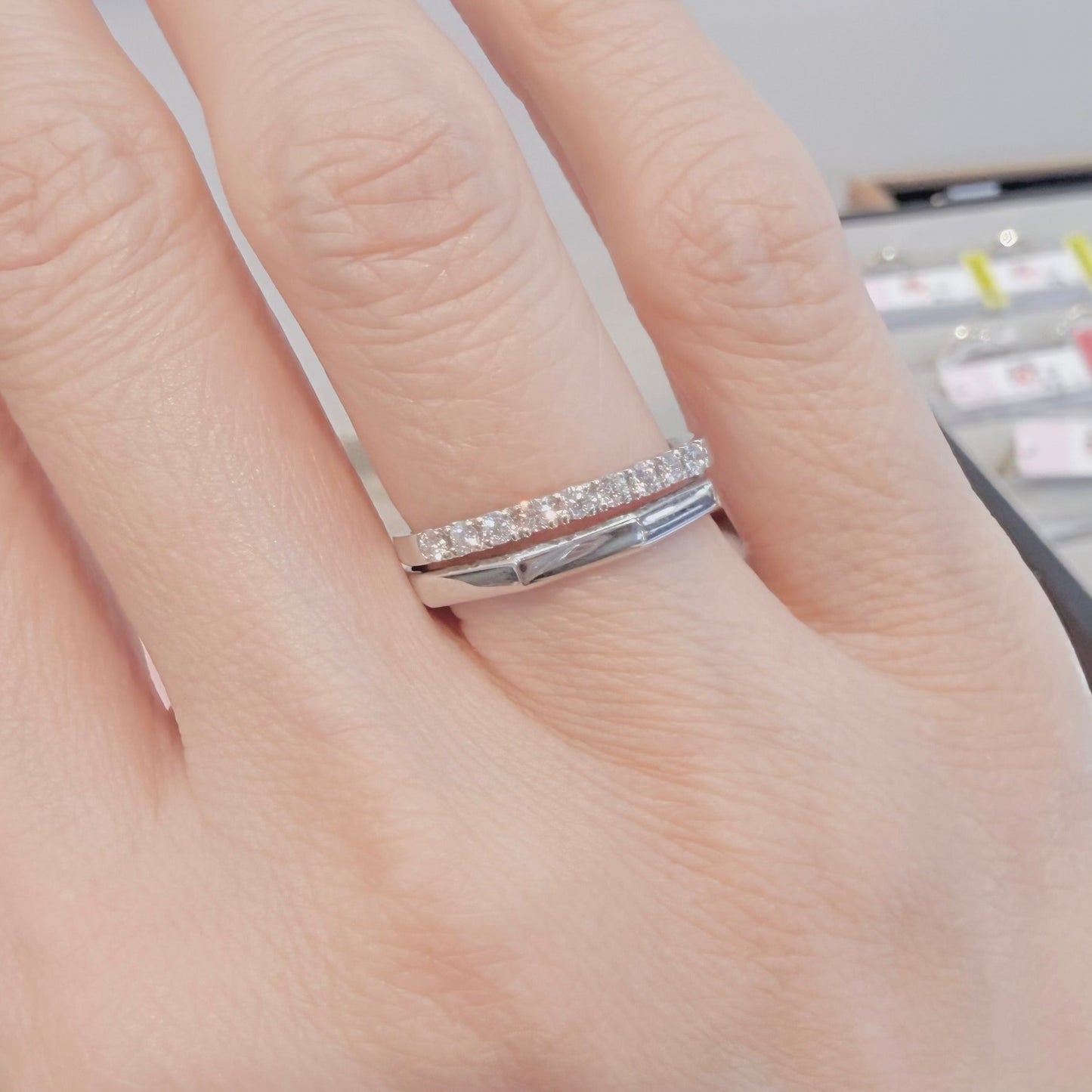 Hand wearing a silver ring with small diamonds on a blurred background