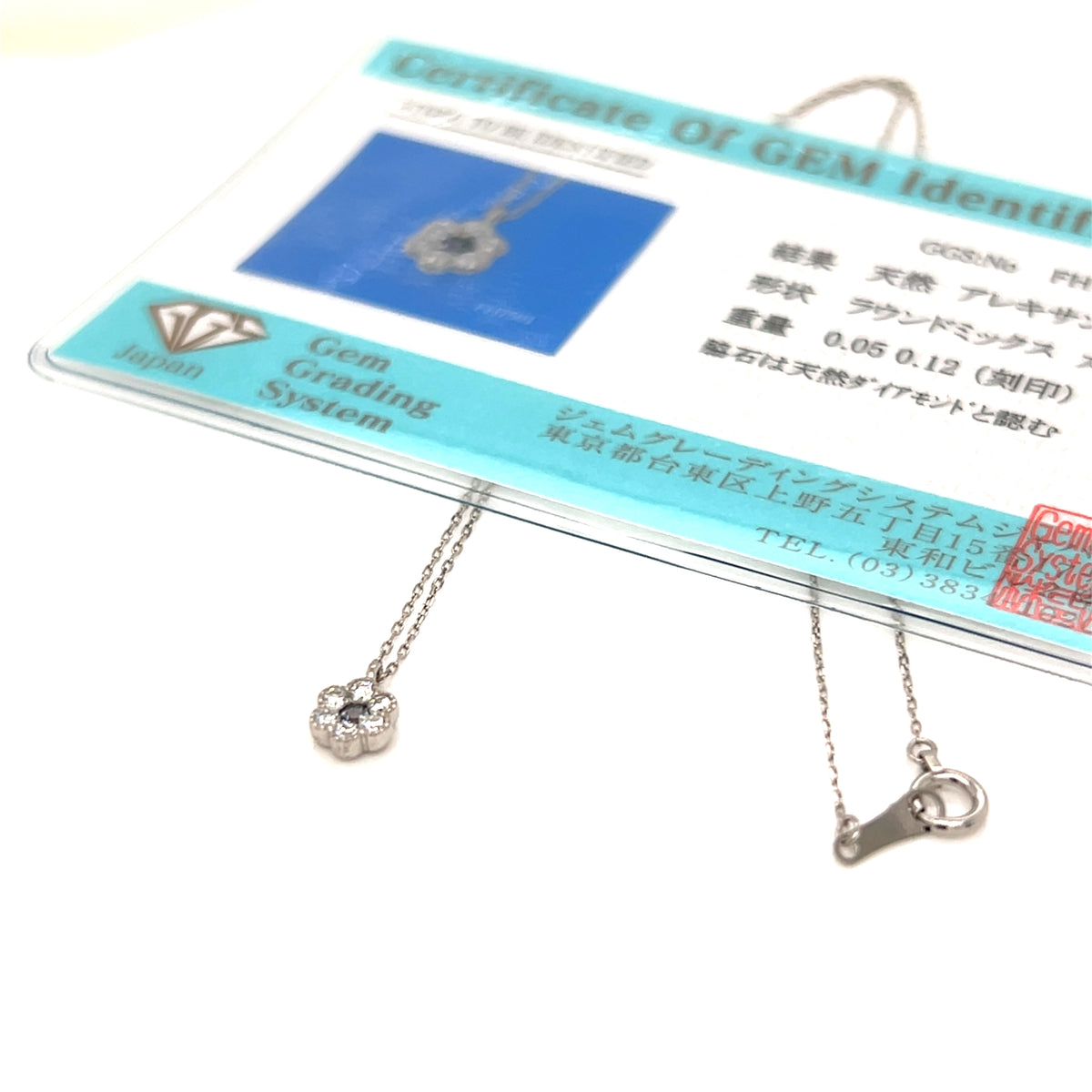 A silver-toned flower-shaped pendant necklace with a matching clasp, displayed on a clear card with a Gem Grading System certificate. The necklace is shown against a plain white background.