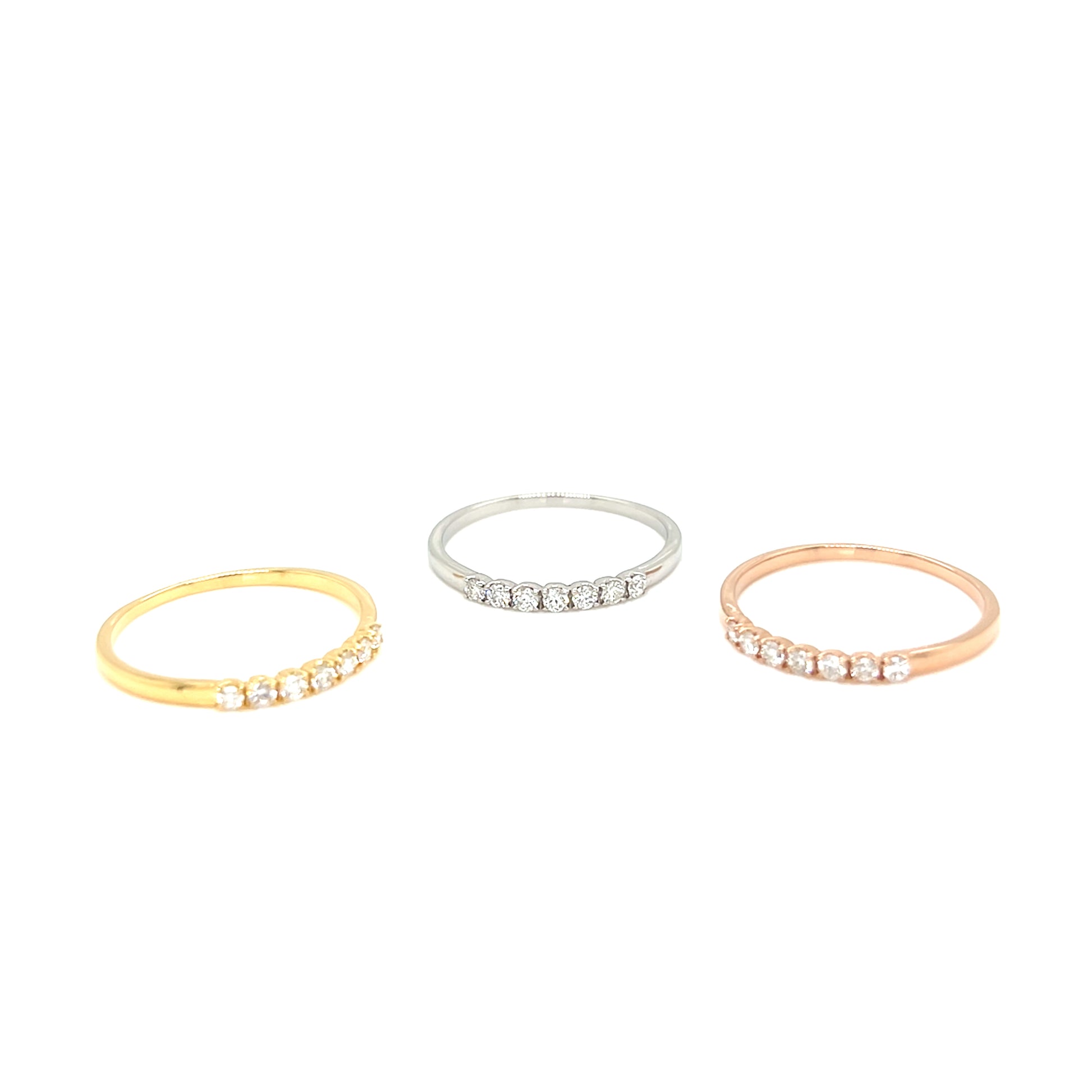 Three slim eternity rings in yellow gold, white gold, and rose gold, each set with small round-cut clear gemstones, displayed on a clean white background.