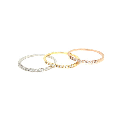 Three slim eternity rings with pavé-set clear stones in silver, yellow gold, and rose gold tones, arranged in a fan shape on a plain white background.