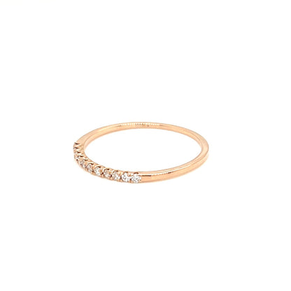 A delicate rose gold ring featuring a row of small clear stones along the front, displayed against a solid white background.