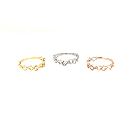 Three delicate rings with small heart-shaped links and clear stones, shown in gold, silver, and rose gold tones on a plain white background.