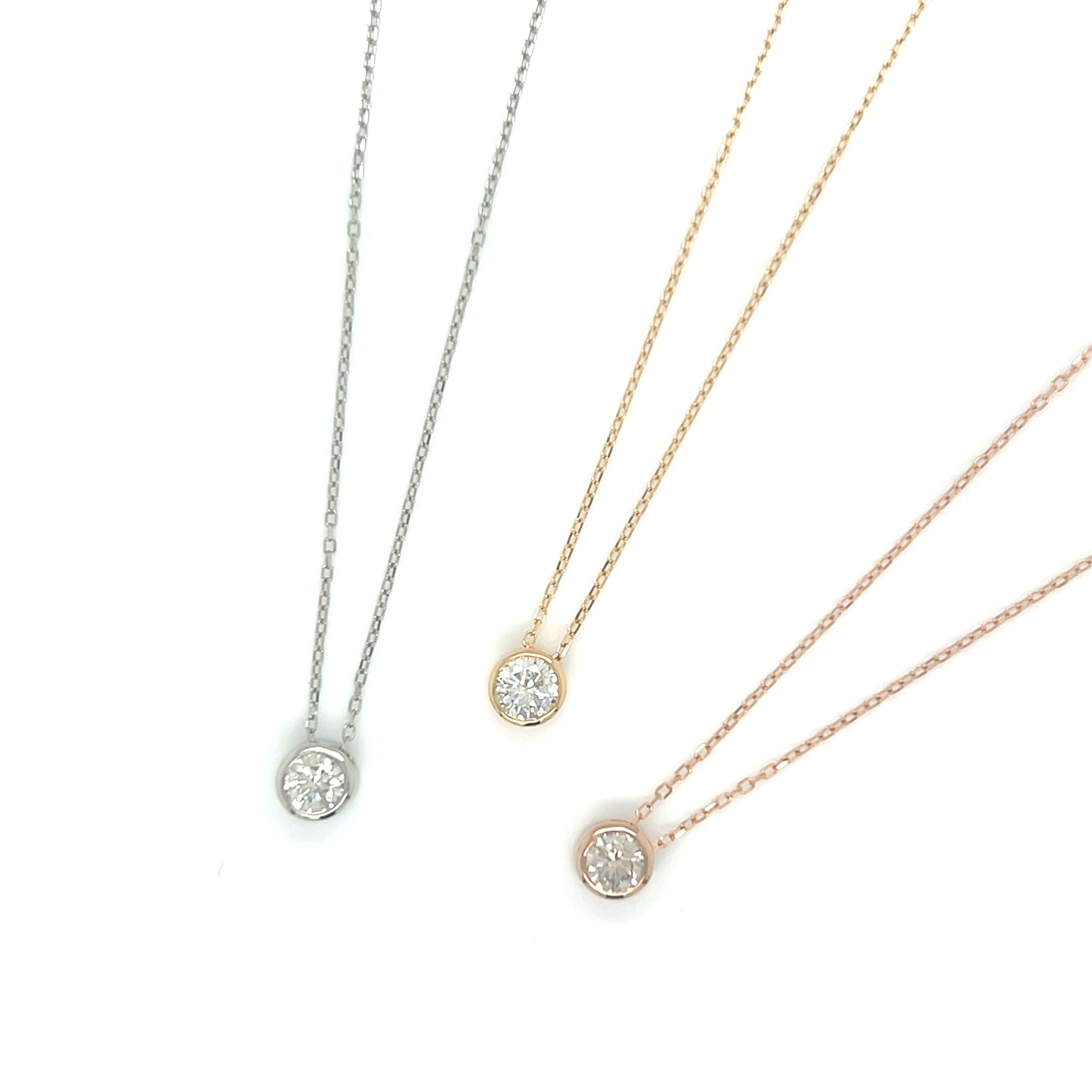 Three pieces bezel diamond necklaces in platinum, gold, and rose gold color on a white background