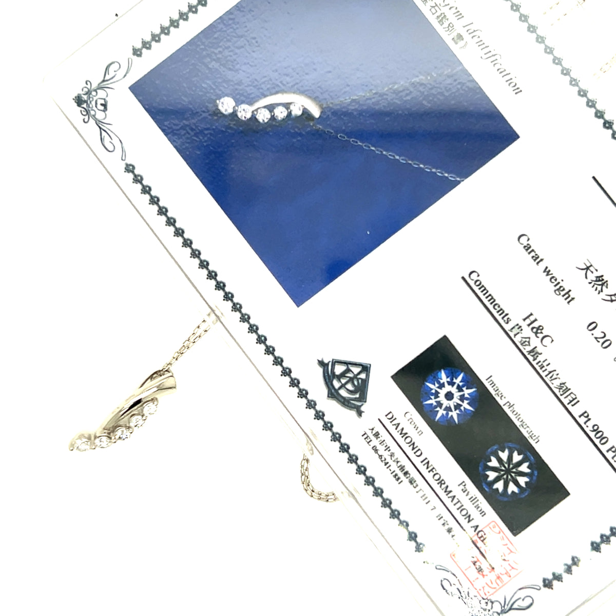 A gold crescent moon necklace with small clear stones is displayed on a white background next to a blue card and a Japanese certificate. The necklace is shown in close-up, with the pendant and chain visible.