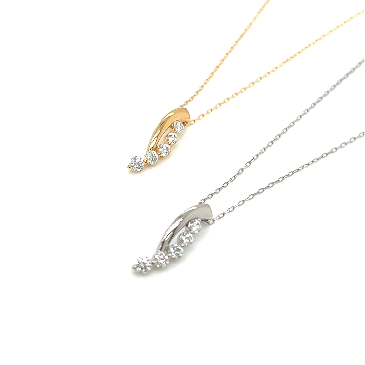 Two curved pendant necklaces on delicate chains, one in yellow gold and one in silver, each featuring a central round stone surrounded by smaller clear stones, shown on a white background.