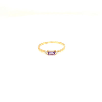 A delicate yellow gold ring featuring a small rectangular purple amethyst gemstone in a bezel setting, flanked by tiny clear accent stones, shown on a plain white background.