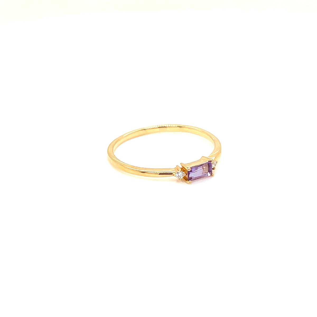 A gold ring featuring a small rectangular purple amethyst center stone and a tiny clear accent stone, set against a plain white background.