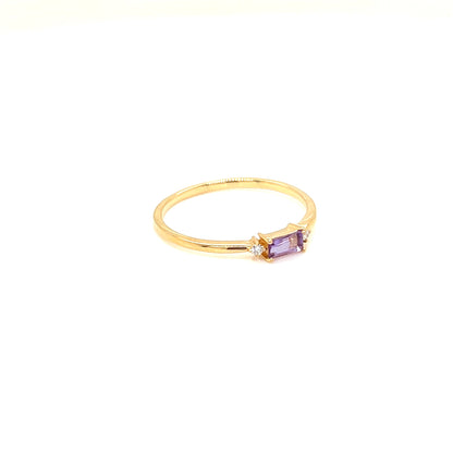 A gold ring featuring a small rectangular purple amethyst center stone and a tiny clear accent stone, set against a plain white background.