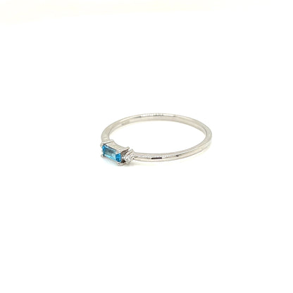 A delicate silver ring featuring a small rectangular blue gemstone in a prong setting, photographed on a clean white background.