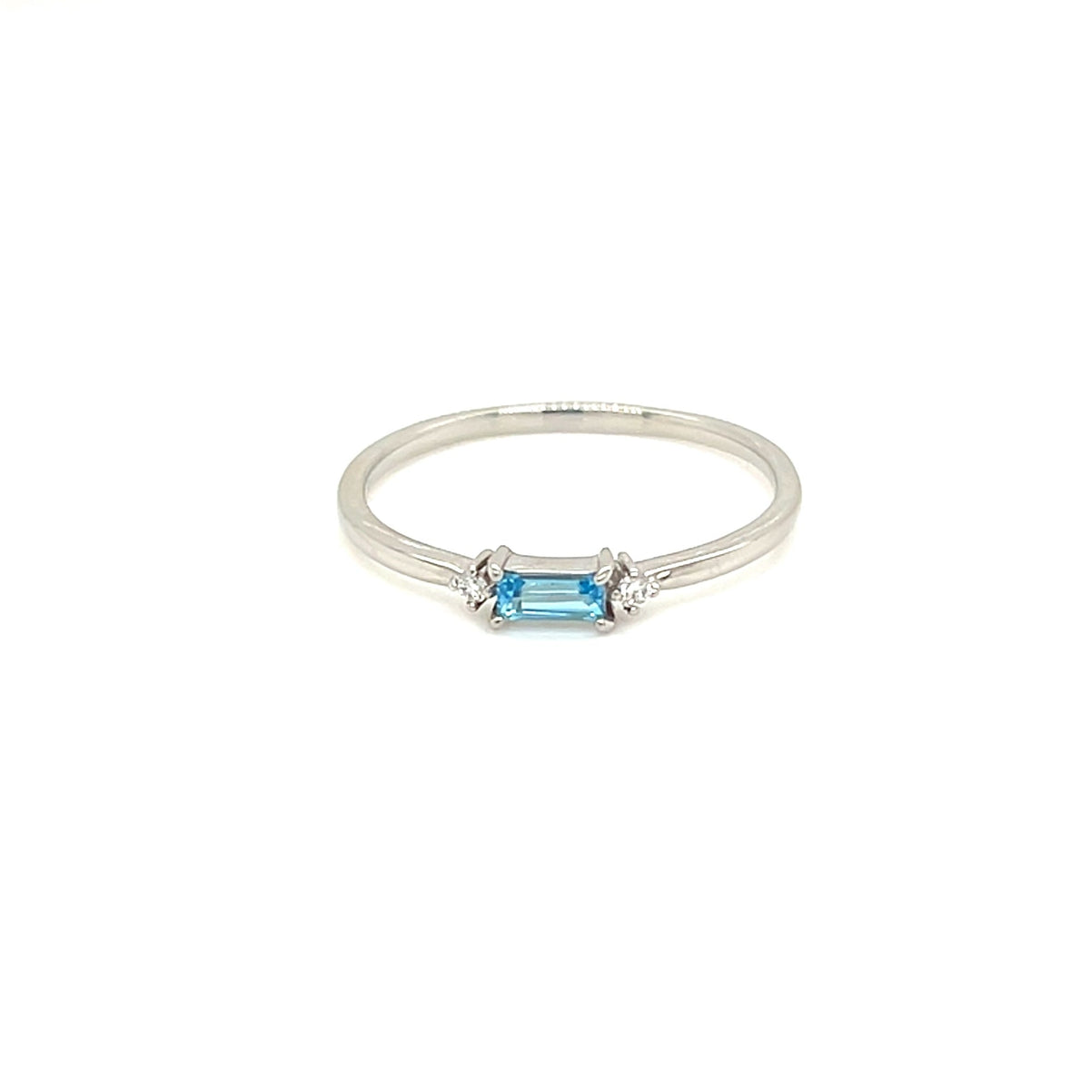 A delicate silver ring featuring a central light blue baguette-cut gemstone, photographed against a solid white background.