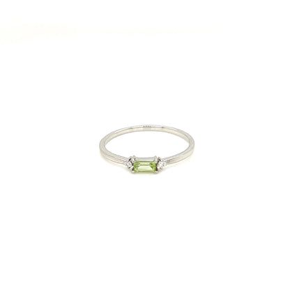 A silver ring featuring a small emerald-cut green gemstone in a prong setting, flanked by two tiny clear accent stones, shown against a plain white background.