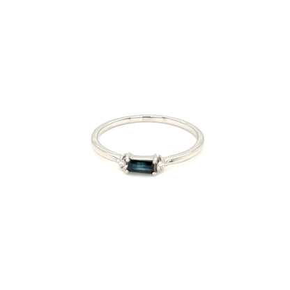 A delicate silver ring featuring a small rectangular dark blue gemstone in a prong setting, centered on a plain white background.