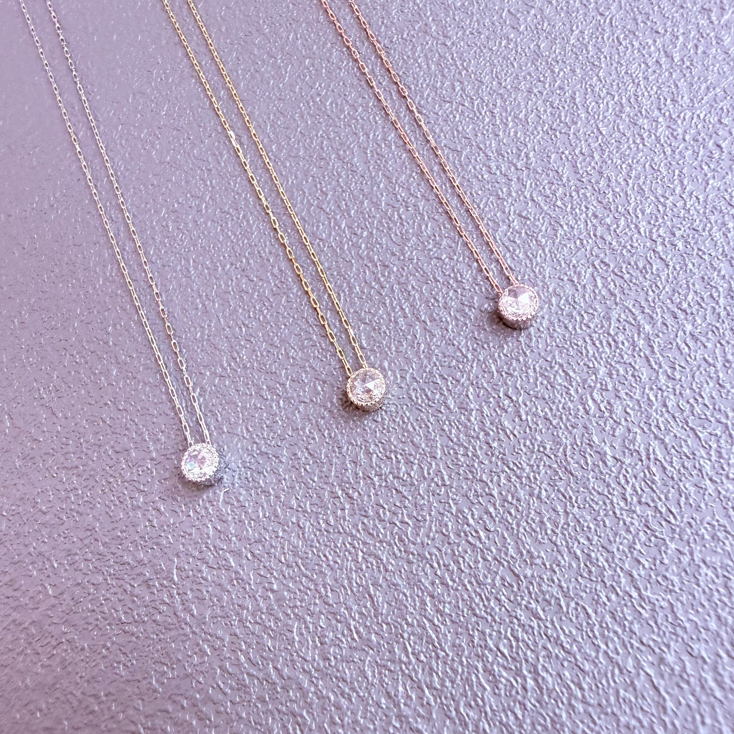 Three gold necklaces with round pendants on a light purple background