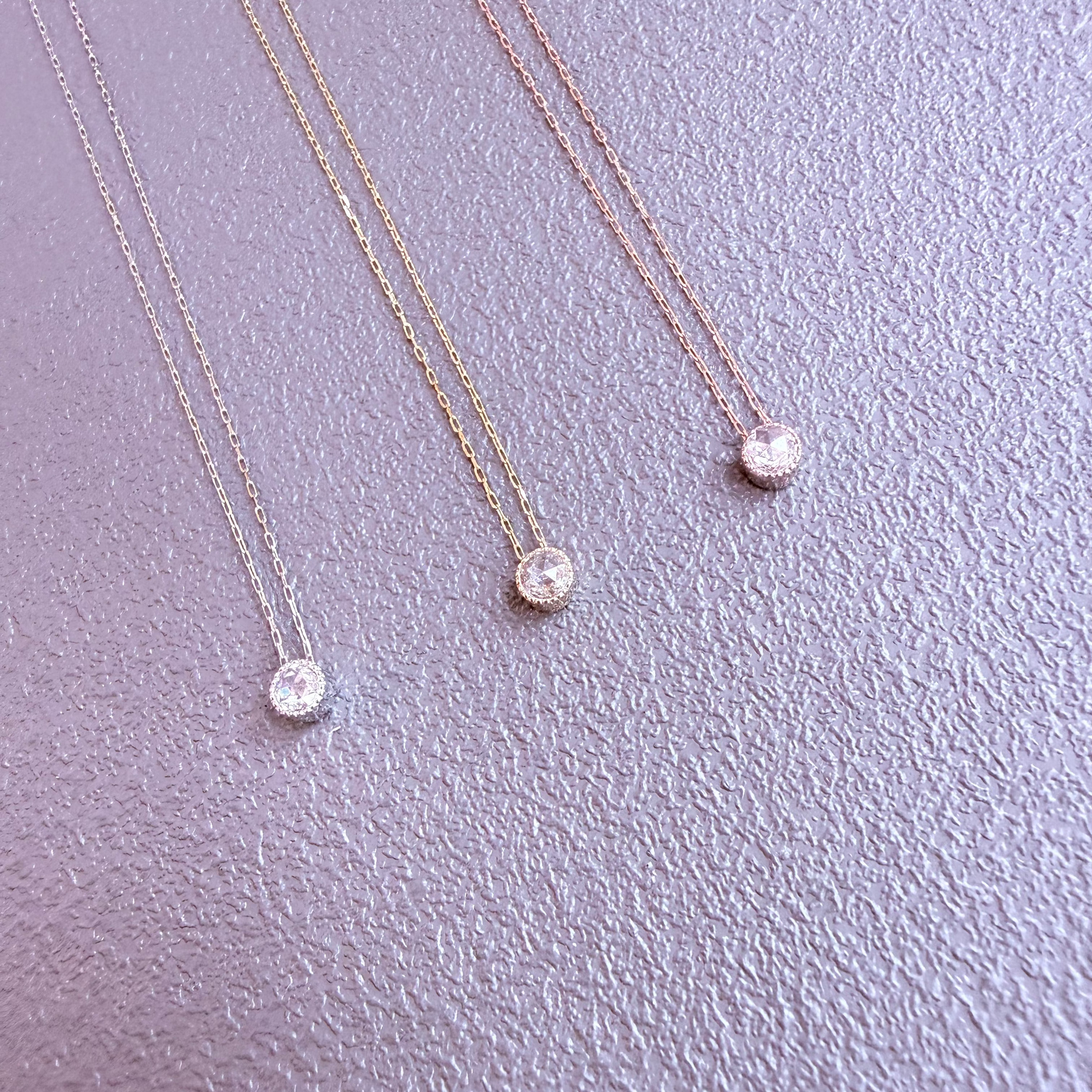 Three gold necklaces with round pendants on a light purple background