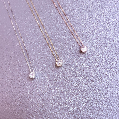 Three gold necklaces with round pendants on a light purple background