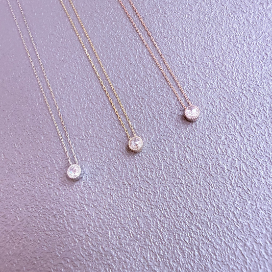 Three gold necklaces with round pendants on a light purple background