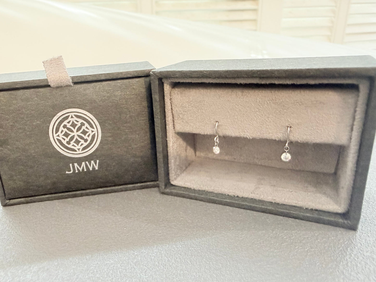 Jewelry box with 'JMW' logo containing a pair of silver earrings.