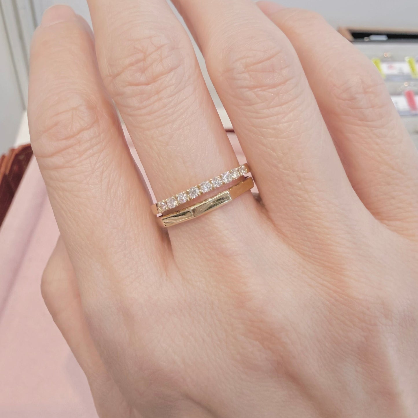 Hand wearing a gold ring with small diamonds on a neutral background