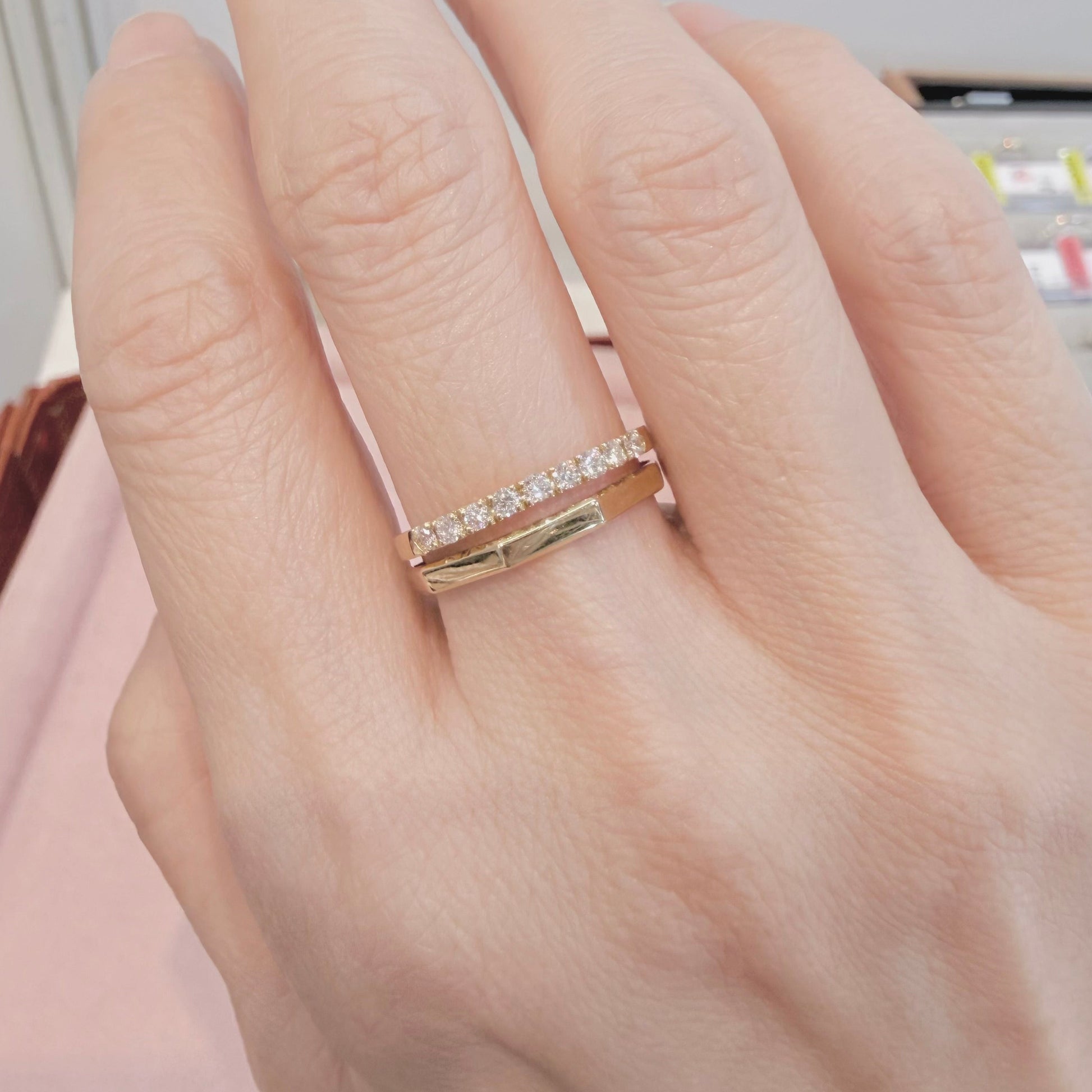 Hand wearing a gold ring with small diamonds on a neutral background