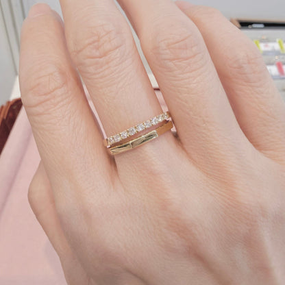 Hand wearing a gold ring with small diamonds on a neutral background