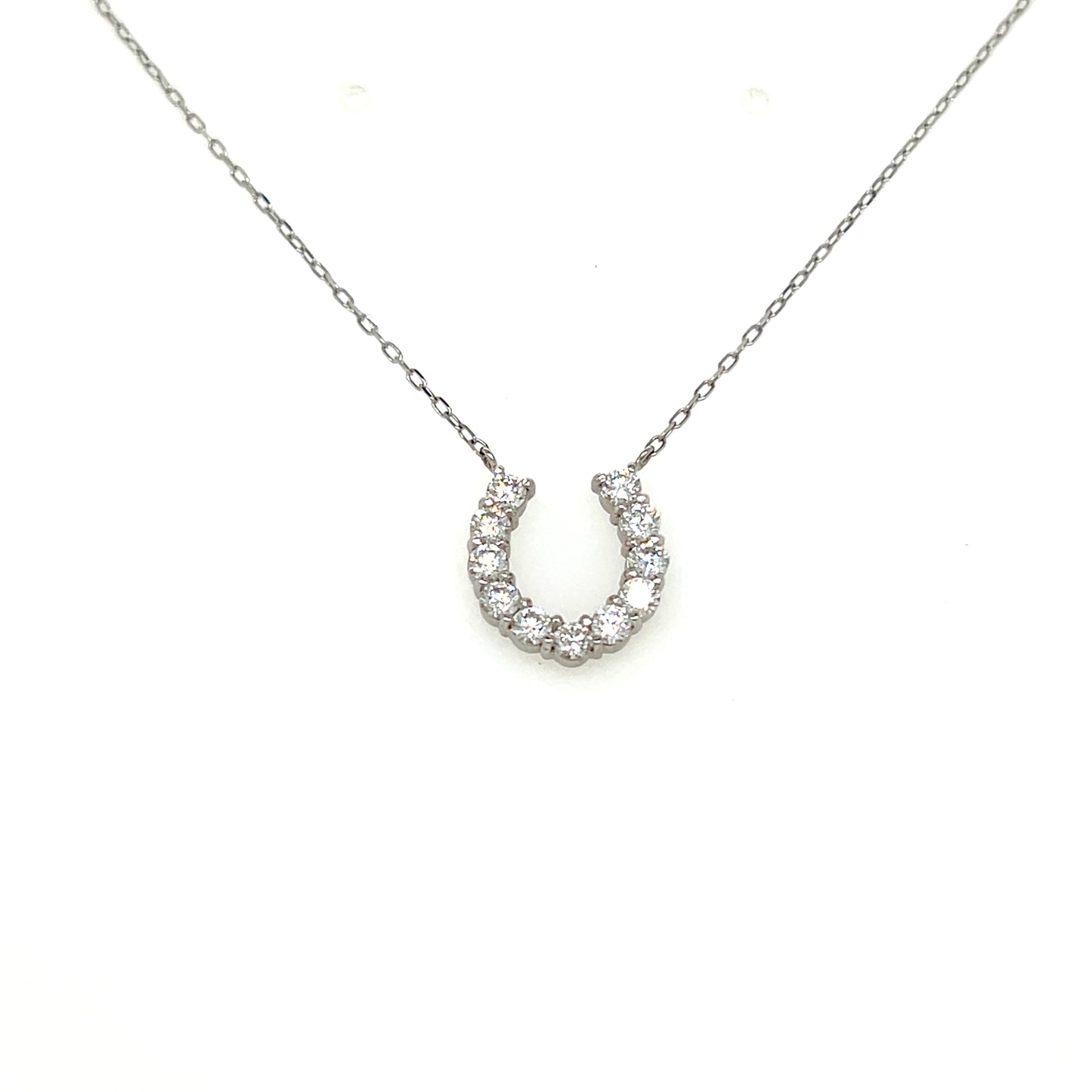 A silver horseshoe pendant necklace set with small clear stones, suspended from a delicate silver chain against a plain white background.