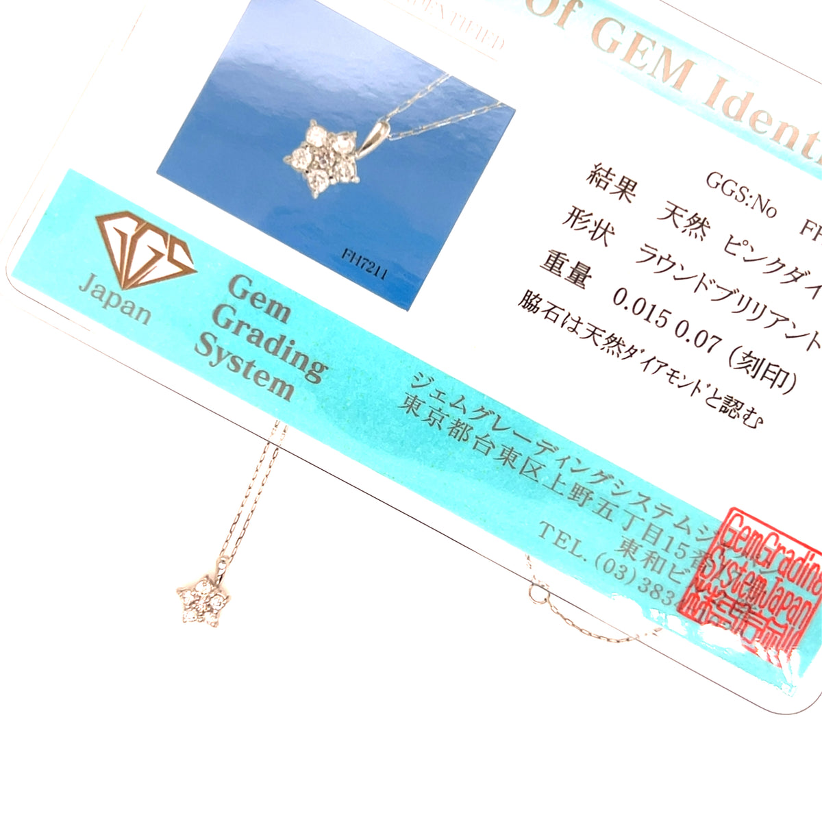 A close-up of a delicate gold-toned pendant necklace with a star and diamond motif, shown draped over its branded Gem Grading System card. The card features a blue inset photo of the necklace, Japanese text, a diamond icon, and a red stamp.
