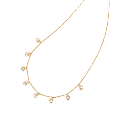 Gold necklace with small dangle bezel diamonds on a white background