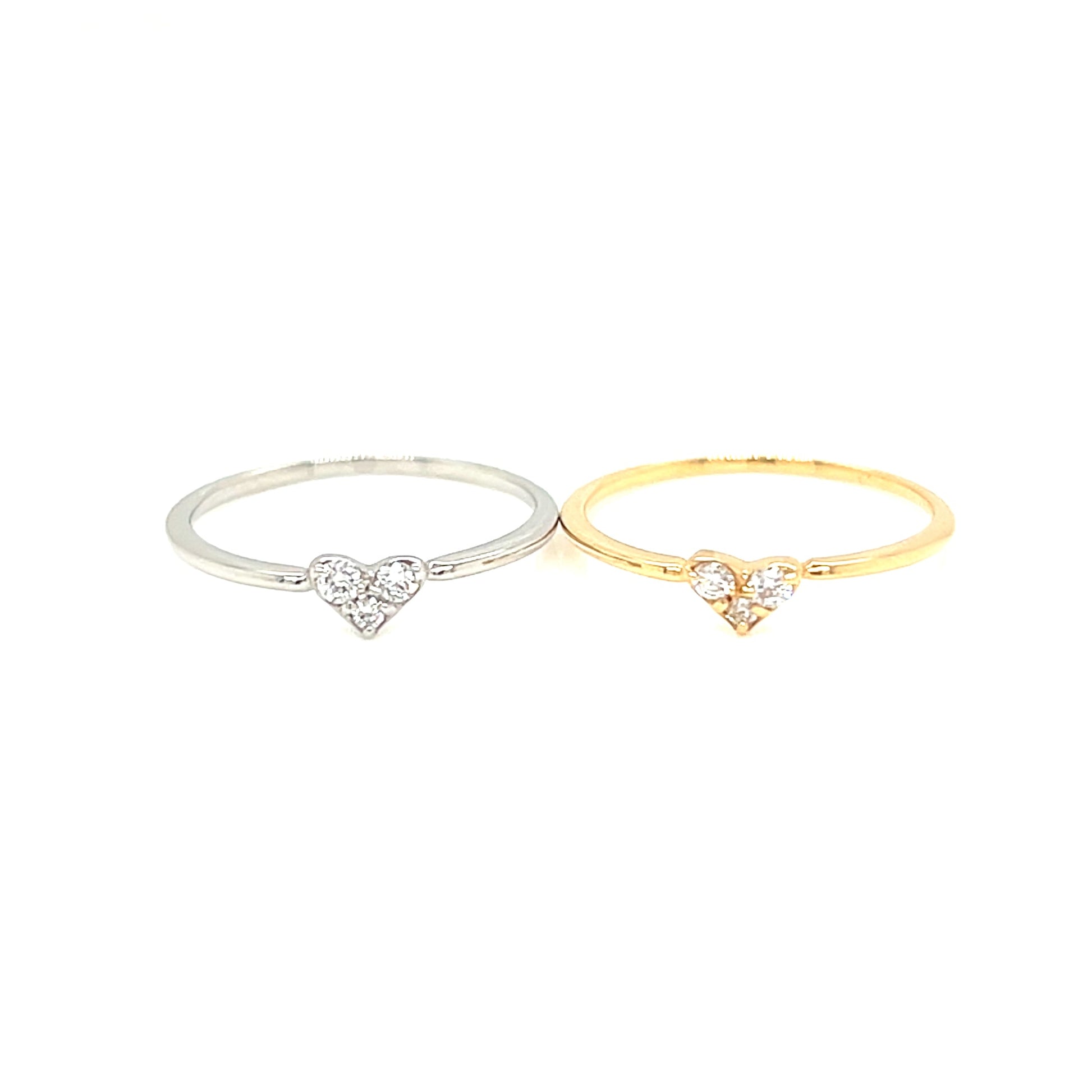 Two slim rings on a white background, one in silver with a small heart-shaped clear stone setting and one in yellow gold with a matching heart-shaped clear stone setting.