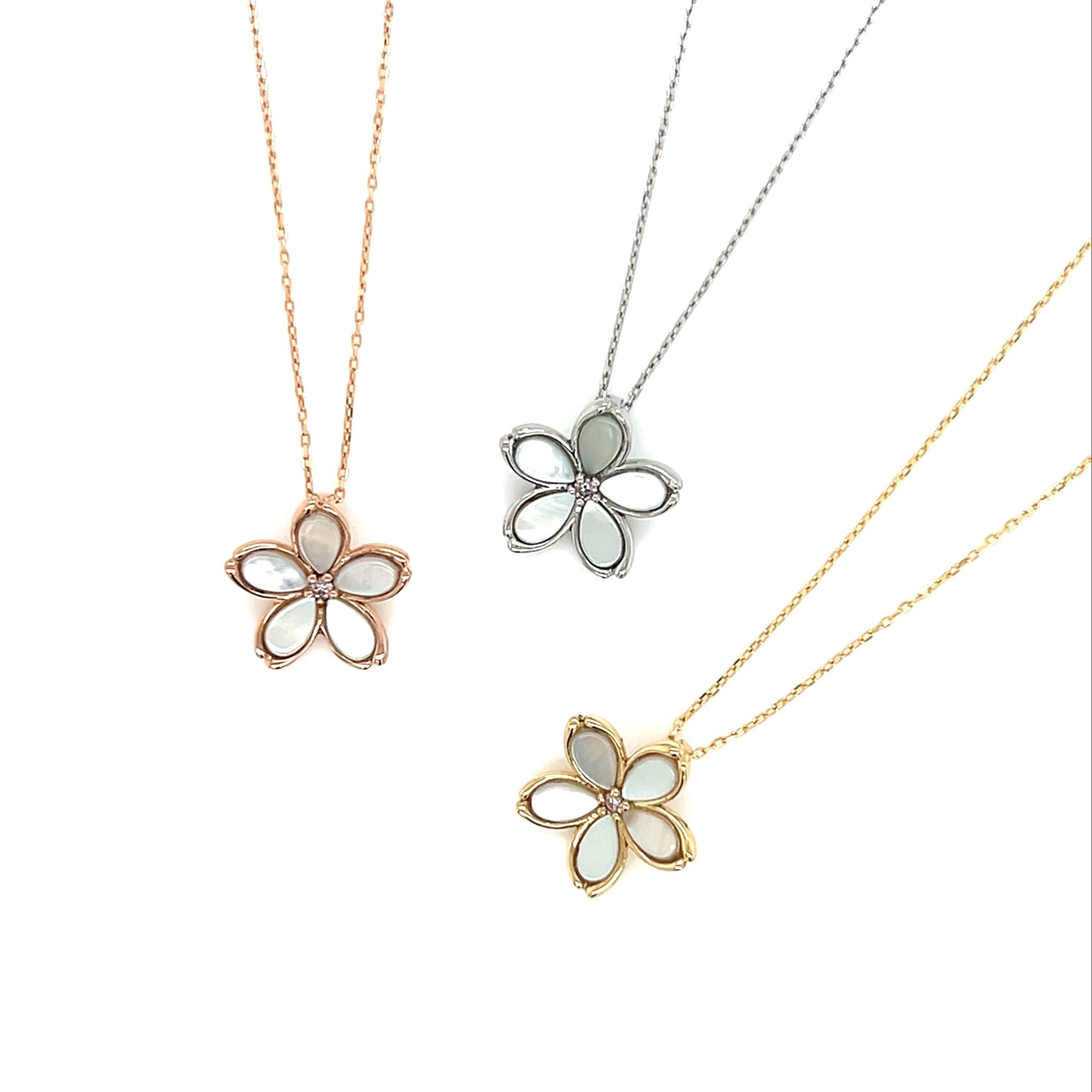Three flower-shaped pendants on necklaces with rose gold, silver, and gold chains on a white background.