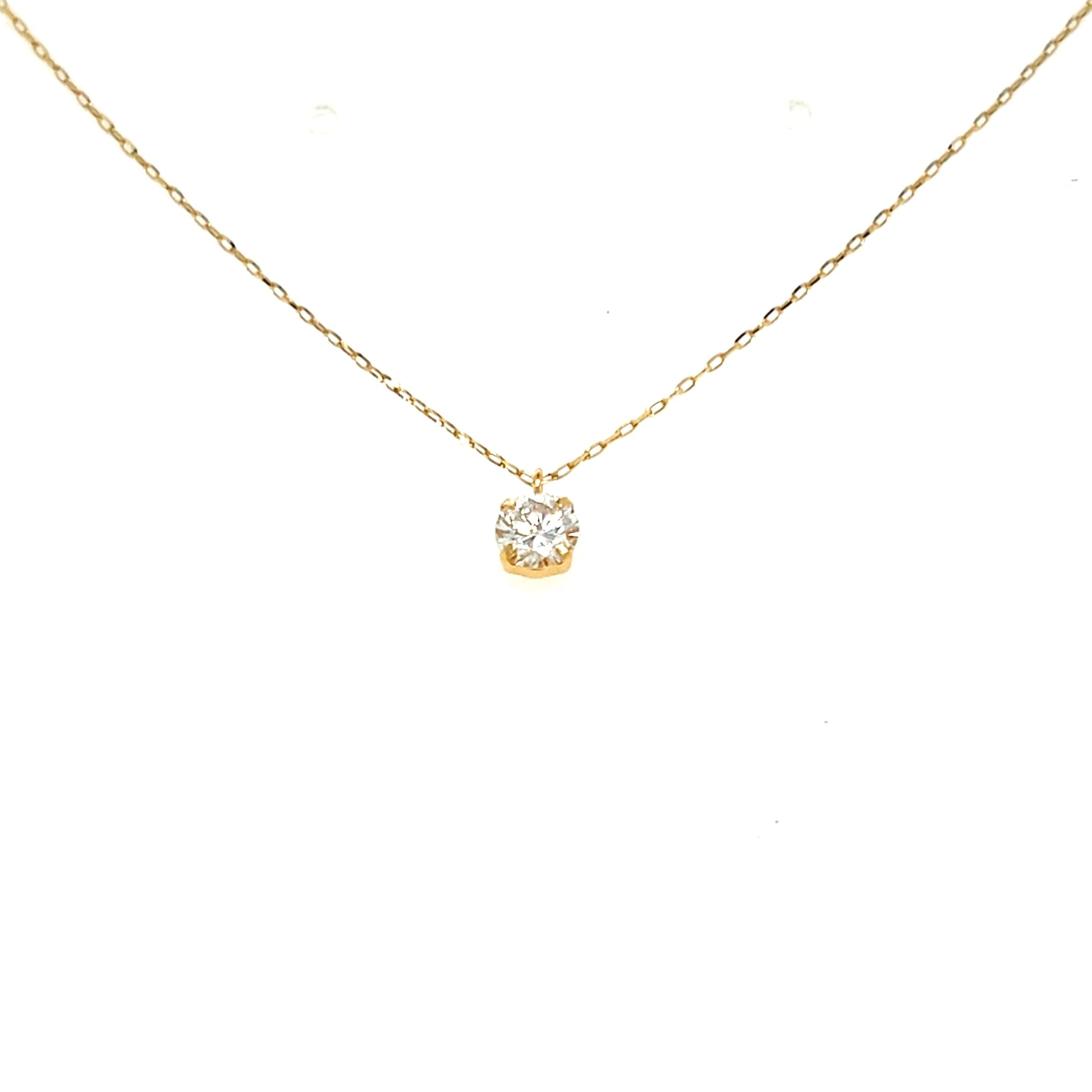A delicate yellow gold chain necklace with a small, round bezel-set clear gemstone pendant, displayed against a solid white background.