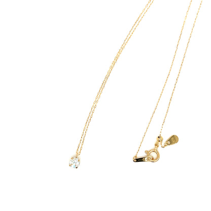 A delicate gold necklace with a small clear gemstone pendant on one side and a gold clasp with a small heart charm on the other, displayed against a solid white background.